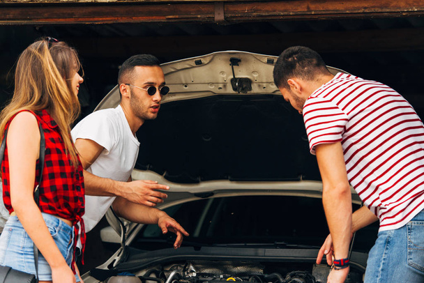 Two guys trying to fix some car troble while a girl is standing next to them - Фото, зображення