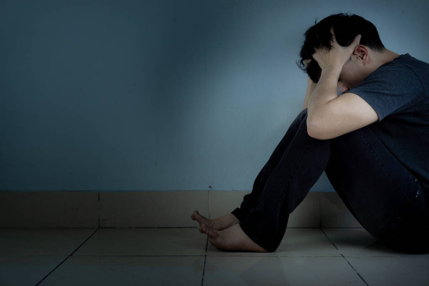 Trauriger Mann umarmt sein Knie und weint allein in einem dunklen Raum sitzend. depre - Foto, Bild