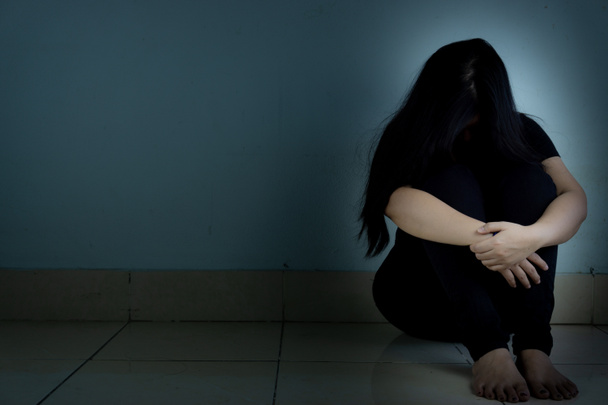 szomorú nő öleli térdét és sír ül egyedül egy sötét szobában. Dep. - Fotó, kép