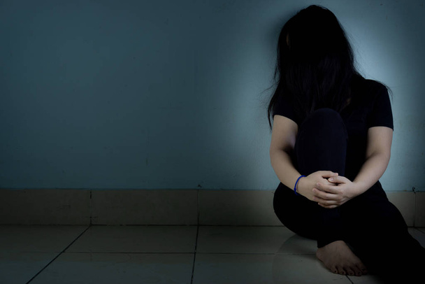 Smutna kobieta przytula kolano i płacze samotnie w ciemnym pokoju. Grupa robocza - Zdjęcie, obraz