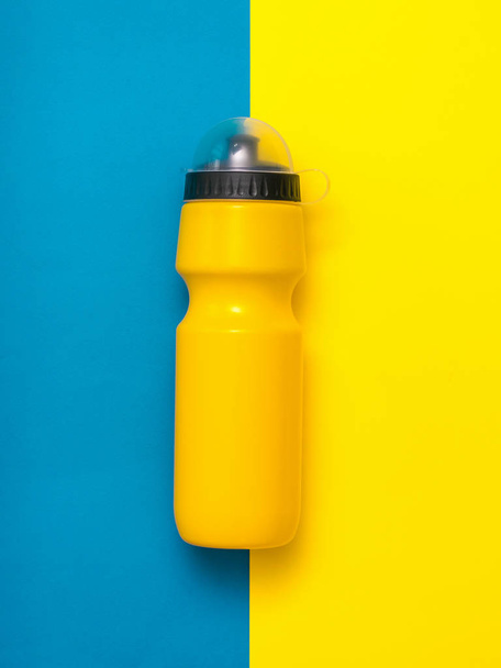 Yellow sports bottle with lid on yellow and blue background. - Photo, Image