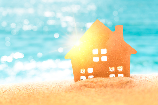 Zamknięte malutkie modele domów na piasku ze światłem słonecznym i tłem plaży. - Zdjęcie, obraz