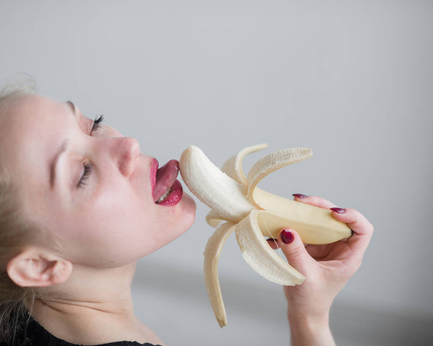 A girl with long blond hair sexually licks a big yellow banana with her tongue. Is oral sex - Foto, Imagen