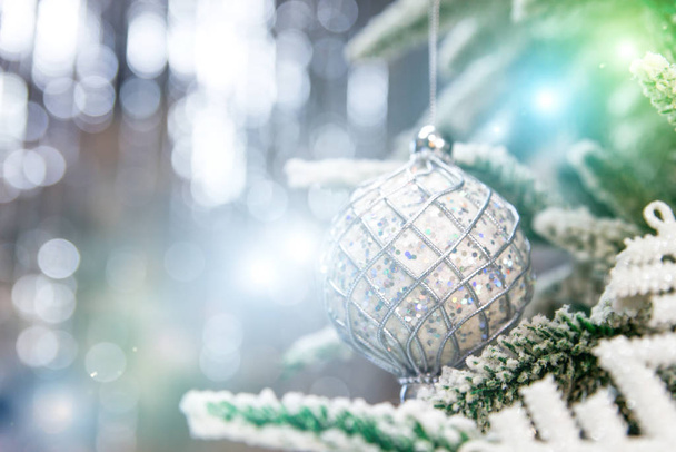 Close up of beautiful christmas decoration- bauble Christmas silver ball hanging on the Christmas tree on the background of bokeh. Silver blue Christmas winter background. Selective focus . - Photo, Image