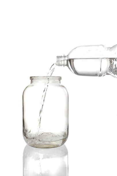 Pouring water into an empty glass jar on a white background - Fotó, kép