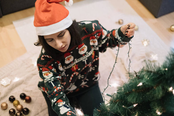 Young woman wrapping tree with Christmas lights - Valokuva, kuva