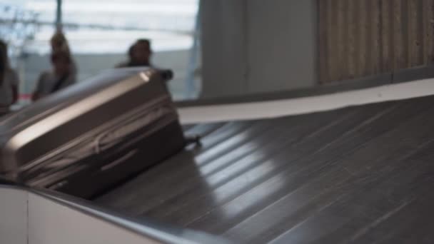 Koffer beweegt langs de transportband op de luchthaven. Silhouetten van mensen 4k - Video