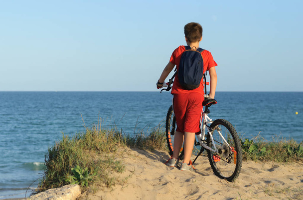 un niño con una bicicleta en una colina mira al mar
 - Foto, Imagen