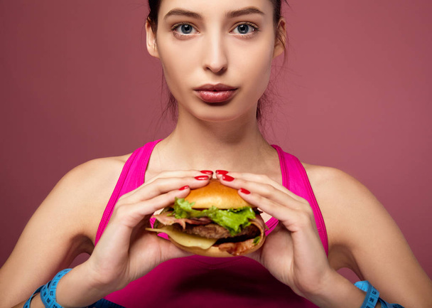 Sad lady on a diet holds a big cheeseburger in her hand. - Photo, Image