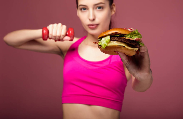 Girl with a burger posing in the gym. - Фото, изображение