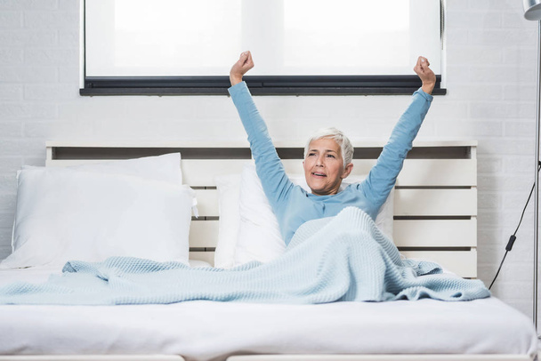 Happy grey hair senior woman stretching in bed after wake up in morning in bed - Foto, imagen