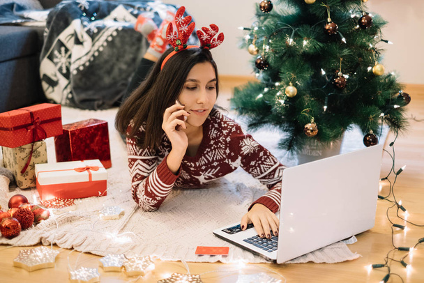 Dívka nakupování on-line pro vánoční dárky, zatímco mluví na telefonu. - Fotografie, Obrázek