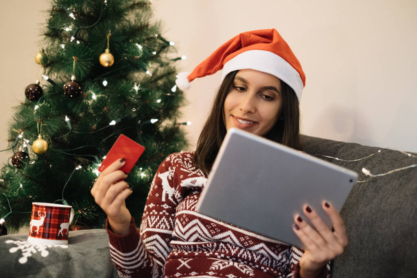 Happy nainen ostoksia verkossa istuu lähellä joulukuusi
 - Valokuva, kuva