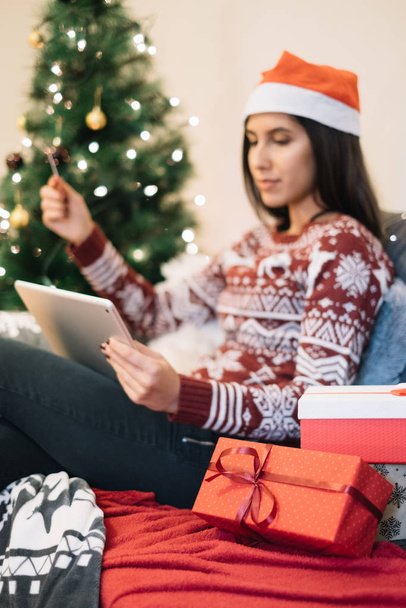 Woman with Santa hat looking for presents on tablet - Фото, изображение