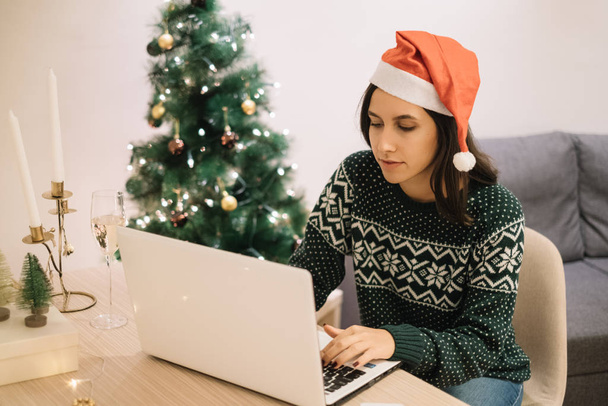 Young woman with Santa hat working on a white laptop - Zdjęcie, obraz