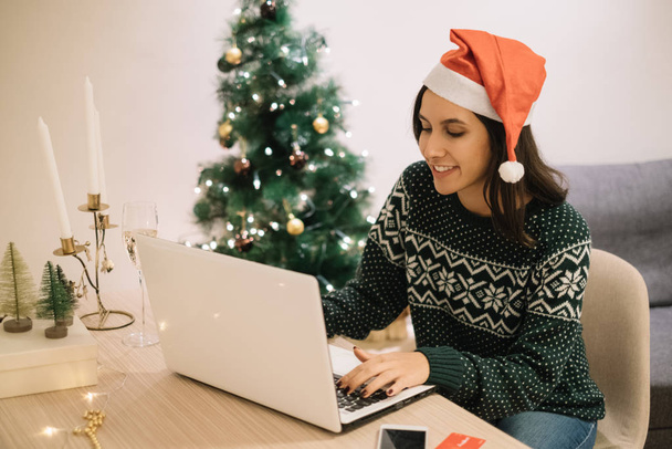 Smiling girl with holiday sweater typing at a white laptop - Фото, изображение
