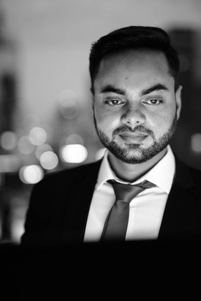 Young bearded Indian businessman against view of the city at night - Фото, зображення