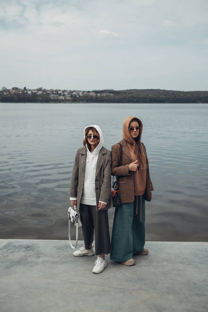 Portret dwóch dziewczyn mody, najlepsi przyjaciele na zewnątrz, noszenie stylowej kurtki, spacery w pobliżu jeziora - Zdjęcie, obraz