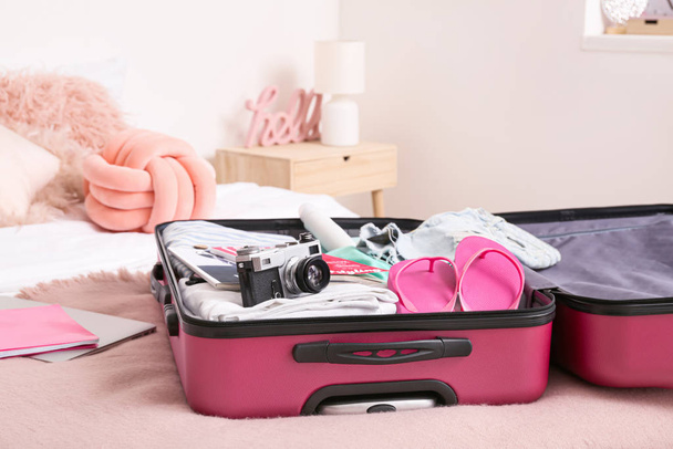 Valise ouverte avec vêtements emballés et accessoires sur le lit
 - Photo, image