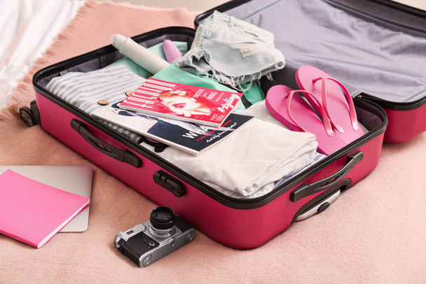 Открытый чемодан с упакованной одеждой и аксессуарами на кровати
 - Фото, изображение