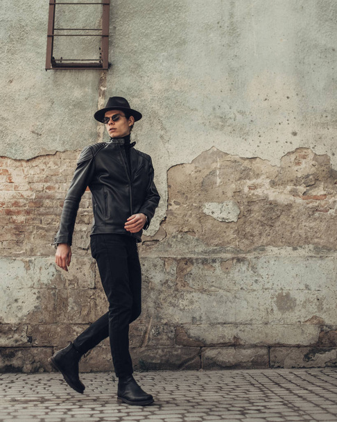 Portret van stijlvolle jonge man in zwart lederen jas en hoed - Foto, afbeelding