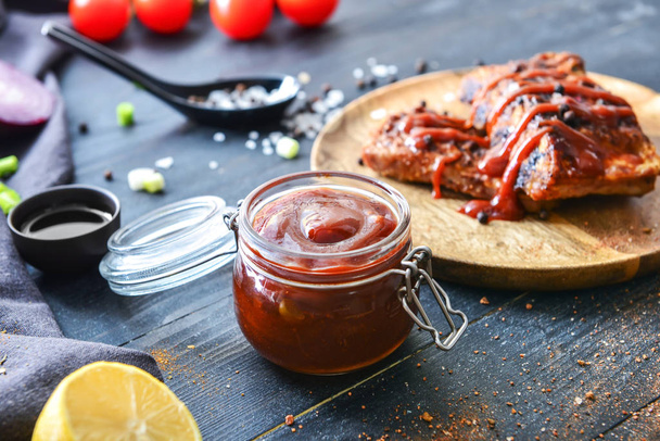 Jar with barbecue sauce and fried meat on dark table - Fotoğraf, Görsel
