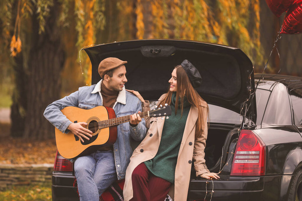 glückliches junges Paar mit Auto und Gitarre, das sich im Park ausruht. Valentinstag-Feier - Foto, Bild
