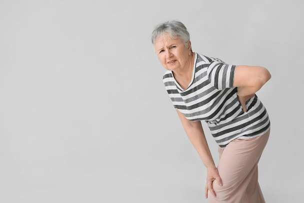 Старшая женщина страдает от болей в спине на сером фоне
 - Фото, изображение