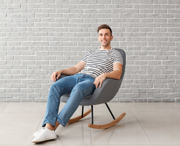 Handsome man sitting in armchair near brick wall - Zdjęcie, obraz