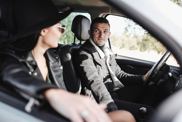 Happy Traveling Couple Dressed in Black Stylish Clothes Enjoying a Road Trip Sitting Inside the Car, Vacation Concept - Фото, изображение