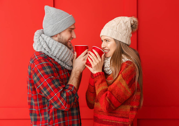 Portrait of happy couple in winter clothes and with cups of hot tea on color background - Foto, afbeelding