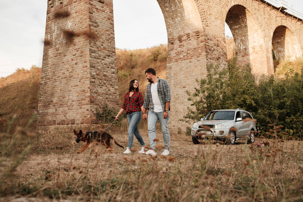 Счастливая пара, путешествующая вместе, наслаждаясь путешествием с собакой, отпуском, отпуском за городом
 - Фото, изображение