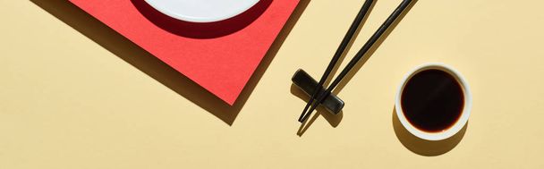 top view of fresh nigiri with salmon near soy sauce and chopsticks on red and beige surface, panoramic shot - 写真・画像