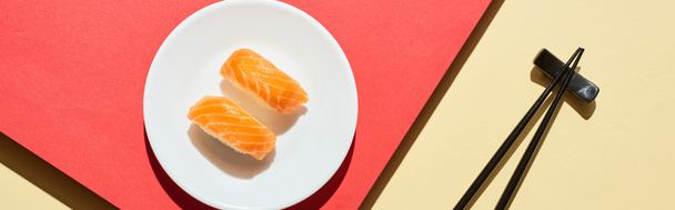 top view of fresh nigiri with salmon near chopsticks on red and beige surface, panoramic shot - Foto, afbeelding