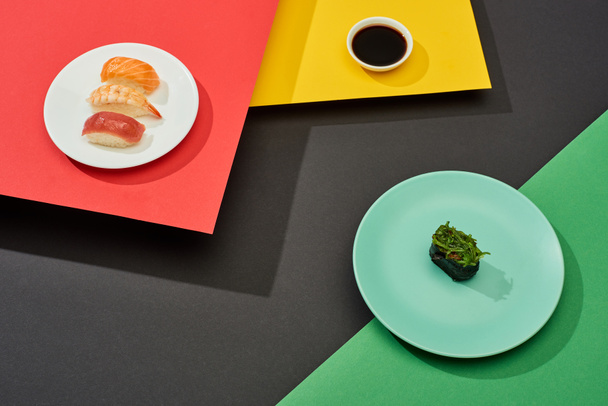 verse nigiri met zalm, garnalen en tonijn bij sojasaus en nigiri met zeewier op rood, geel, groen en zwart oppervlak - Foto, afbeelding