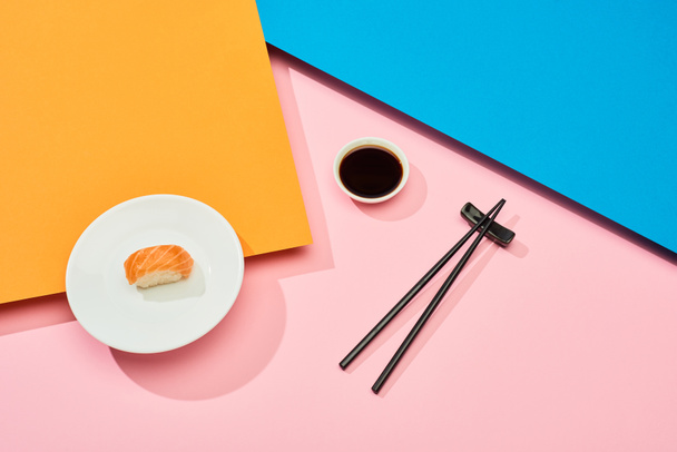 fresh nigiri with salmon near soy sauce and chopsticks on blue, pink, orange surface - 写真・画像