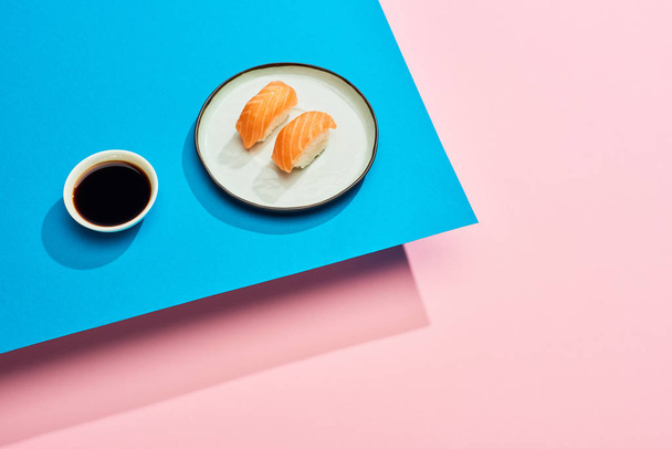 φρέσκο nigiri με σολομό κοντά σάλτσα σόγιας σε μπλε, ροζ φόντο - Φωτογραφία, εικόνα