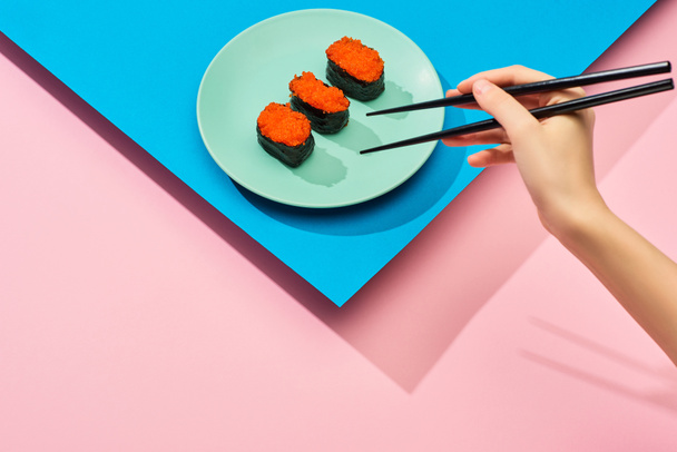cropped view of woman eating fresh nigiri with red caviar on blue, pink background - Fotó, kép