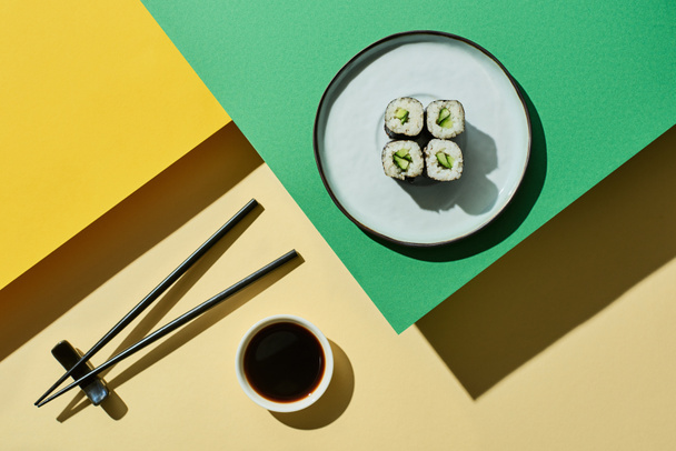 top view of fresh nigiri with cucumber near soy sauce and chopsticks on green and yellow surface - Photo, Image