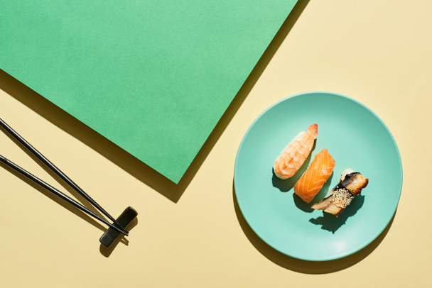 top view of fresh nigiri with salmon, shrimp and eel near chopsticks on green and yellow surface - Photo, Image
