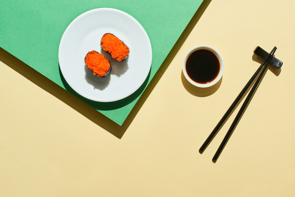 top view of fresh nigiri with red caviar near soy sauce and chopsticks on green and yellow surface - 写真・画像