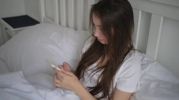 Young woman staying in bed on her day off and using mobile - Video, Çekim