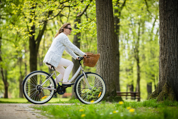 Woman in white outfit riding bicycle in spring park - Fotoğraf, Görsel
