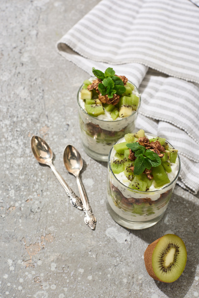fresh granola with kiwi and yogurt on grey concrete surface with striped napkin and spoons - Foto, Bild