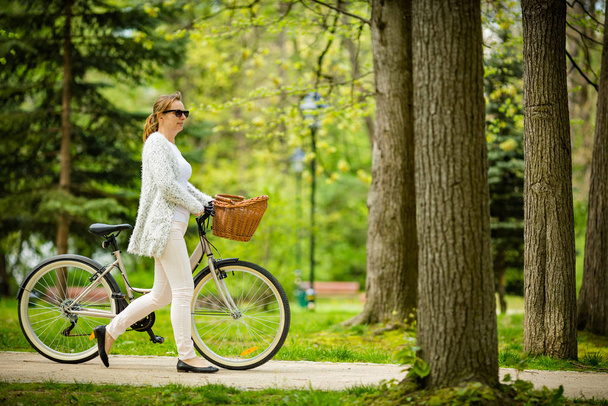 Woman in white outfit riding bicycle in spring park - Photo, image