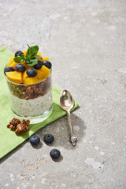 fresh granola with canned peach, blueberries and chia seeds on grey concrete surface with napkin and spoon - Foto, afbeelding