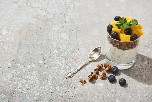 fresh granola with canned peach, blueberries and chia seeds on grey concrete surface with spoon - Photo, Image