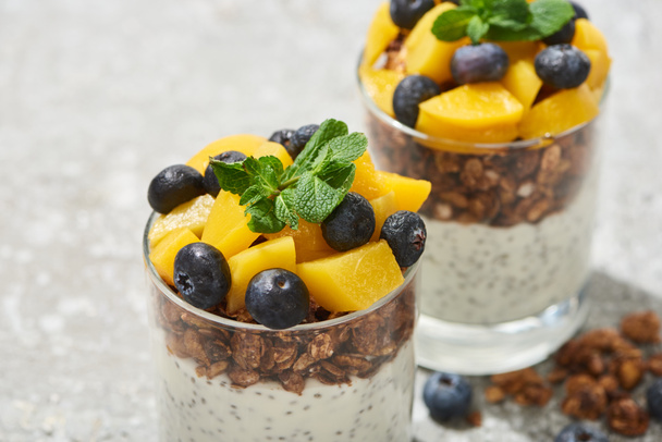 close up view of tasty granola with canned peach, blueberries and yogurt with chia seeds on grey concrete surface - Photo, Image