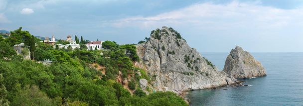 Costa del mar con rocas escarpadas, pueblo costero entre los árboles
 - Foto, Imagen