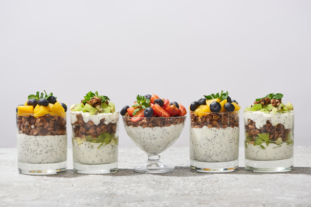 delicious granola in glasses with fruits and berries on grey concrete surface isolated on white - Фото, изображение